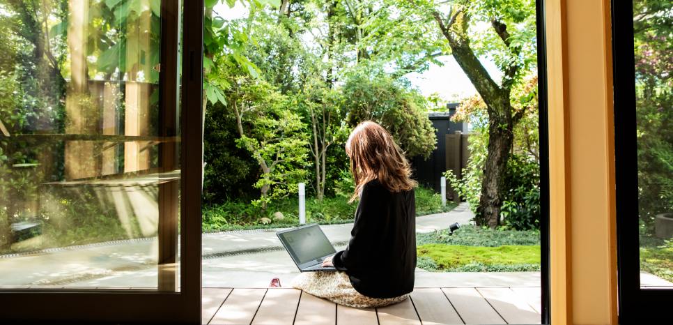 A woman working on a laptop in a serene tree-filled garden.