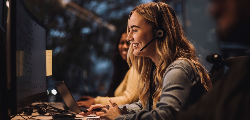 A smiling woman wearing a headset working on a computer in an office.